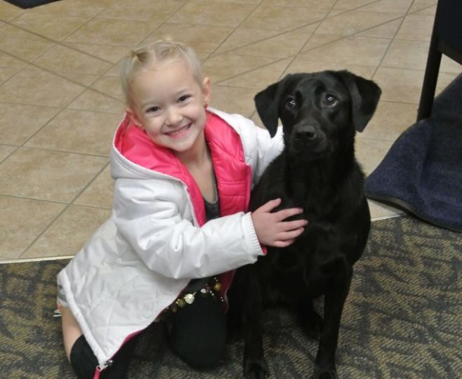 A girl hugging a black dog