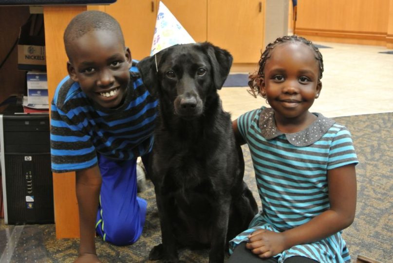 Two children with a dog wearing a birthday hat